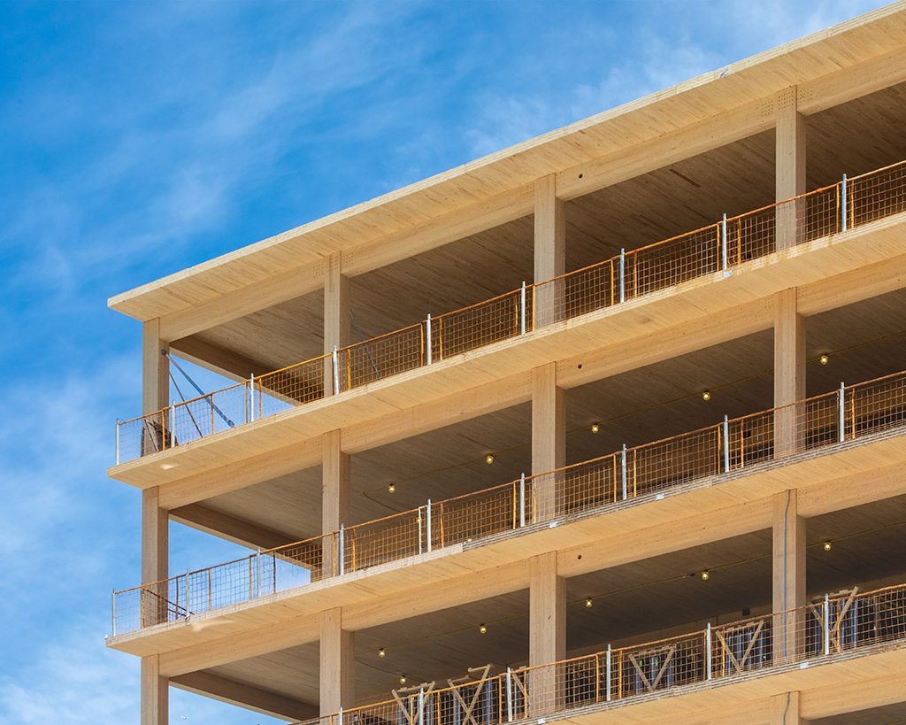 Looking up at the wooden balconies, the vertical supports and interior ceilings of a engineered timber multi story green, sustainable residential high rise apartment building construction project
